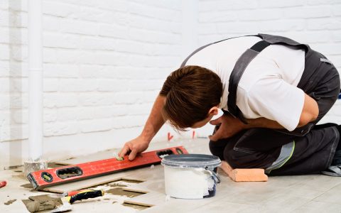 Builder checks the quality of the laid tiles with a manual bubble level. Construction worker installing ceramic floor tiles on construction sites. Floor repair. selective focus