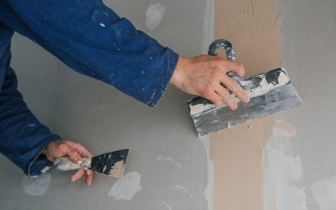 plasterer man works plastering two trowels on plasterboard in blue uniform