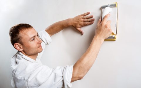 Professional worker grinding white wall with sandpaper. Copy space.